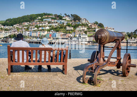 23. Mai 2018: Dartmouth, Devon, UK-Paar auf einer Bank sitzen neben einer alten Kanone, mit Blick auf den Fluss Dart. Stockfoto