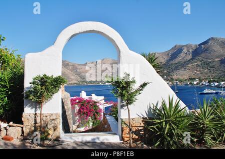 Einen weißen Torbogen frames Livadia Hafen auf der griechischen Insel Tilos am 12. Juni 2018. Stockfoto