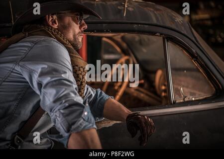 Kaukasische Cowboy Classic Cars Collector. Portrait von Männern und Alten rostigen Fahrzeug in der Scheune. Stockfoto