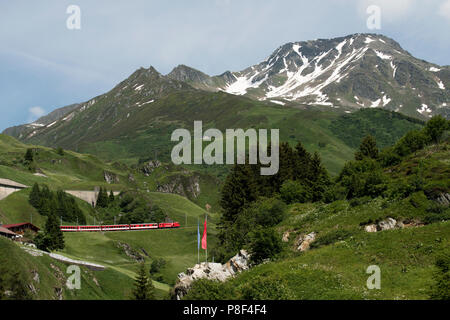 Andermatt im Kanton Uri, Schweiz, an denen Schweizer Berg Züge bis Klettern in Richtung Oberalppass und schweizer Fahnen. Juni 2018 Andermatt ist ein m Stockfoto