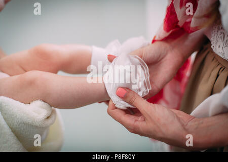 Mama bringt weiße Socken auf die Beine eines kleinen neugeborenen Babys. Stockfoto