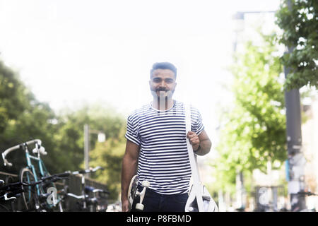 Lächelnd Mann auf der Straße mit einem Skateboard Stockfoto