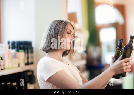 Frau, die in einem Supermarkt vergleichen Flaschen Olivenöl Stockfoto