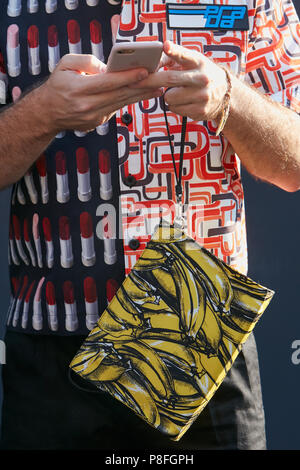 Mailand - 17. Juni: Mann mit roten und weißen Prada shirt auf Smartphone und Tasche mit Bananen vor Prada fashion show, Mailand Fashion Week Straße st Stockfoto