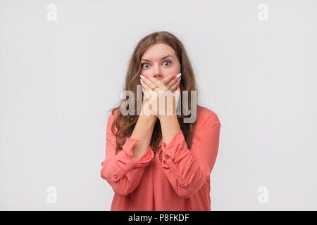 Close up Portrait von attraktiven, kaukasische Frau in Rot shirt ihr Gesicht schließen mit den Fingern. Sie ist besorgt. Sie kann nichts sagen. Eine schlechte Nachrichten Stockfoto