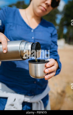Frau strömenden heißen Tee aus einer Thermoskanne an einem Sandstrand an einem sonnigen Tag. Close Up. Stockfoto
