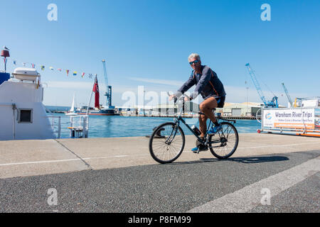 Ein Mann mittleren Alters mit Sonnenbrille Radfahren entlang Poole Quay an einem schönen warmen, sonnigen Sommern morgen, Juni 2018, Poole, Dorset, Großbritannien Stockfoto