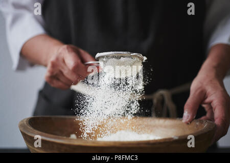 Weibliche Hände Mehl in Schüssel sieben. Stockfoto