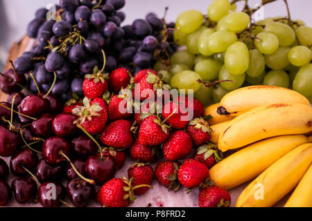 Früchte (weiße und blaue Trauben, Bananen, Erdbeeren und Kirschen) auf einer Holzplatte Stockfoto