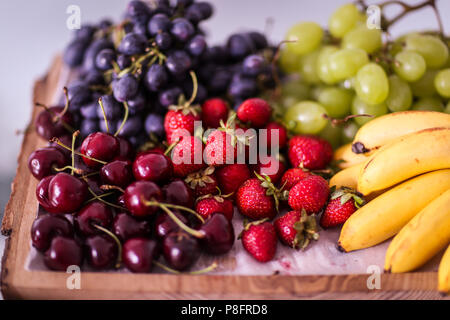 Früchte (weiße und blaue Trauben, Bananen, Erdbeeren und Kirschen) auf einer Holzplatte Stockfoto