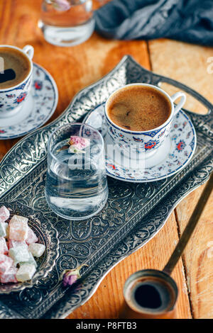 Türkischer Kaffee serviert in einem traditionellen türkischen Kaffee Tasse in einem Kupfer Fach. Ein Glas Wasser mit einem Rosenblütenbad und türkischen Köstlichkeiten auf der Seite. Stockfoto
