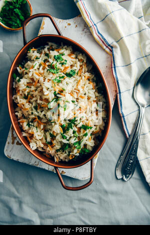 Gebratener Reis Pilav mit orzo in einem Kupfer serviert pan auf eine weiße Tafel. Löffel, weisse Serviette und eine kleine Schüssel mit gehackter Petersilie begleiten. Stockfoto