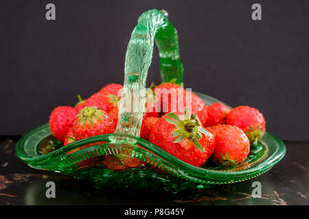 Saftige frische rote Erdbeeren im Vintage grünes Glas Warenkorb auf rustikale Metall Tisch auf schwarzem Hintergrund Stockfoto