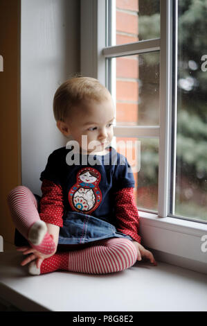 Zwei Jahre altes Kleinkind Mädchen sitzt am Fenster Stockfoto