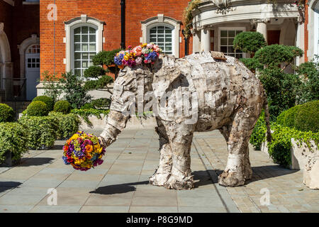 Skulptur eines Asiatischen Elefanten bedeckt mit Streifen aus Rinde und mit hellen Blumen im Garten, in der Nähe des Eingang des Lalit Hotel Stockfoto