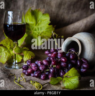 Stillleben von Trauben in einer Urne mit einem Glas Rotwein Stockfoto