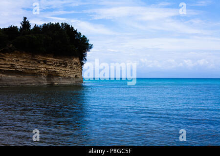 Sedimentäre natürlichen harten Stein Bildung mit Vegetation über die Oberseite in das ruhige Meer durch Wasser in einer sonnigen, blauen Himmel Landschaft umgeben, Me Stockfoto