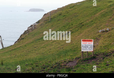 Ein hysterischer Schild mit der Aufschrift "PRIVATEIGENTUM", "KEEP OUT!", "KEINE ÜBERTRETUNG", "GIFT LAID", "ELECTRIC FENCING", "DANGEROUS ANIMALS" auf einer Meeresklippe Stockfoto