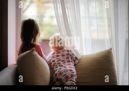 Zwei kleine Mädchen im Schlafanzug Blick aus dem Fenster Stockfoto