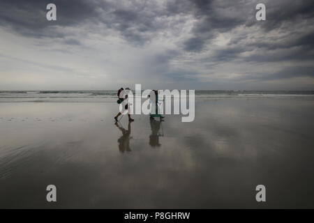 Wanderer Wandern auf einem nassen Strand mit ihrer Reflexion auf dem Sand. Stockfoto