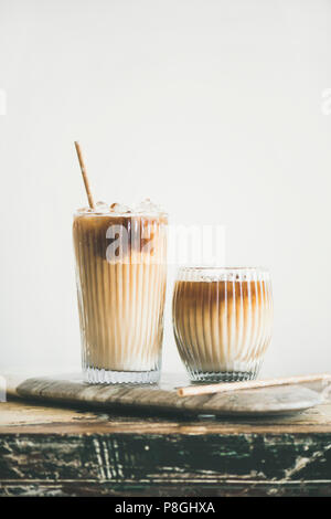 Eiskaffee in hohe Gläser mit Milch und Strohhalme an Bord, weiße Wand im Hintergrund, kopieren. Sommer erfrischende Getränke Eis Kaffee trinken Konzept Stockfoto