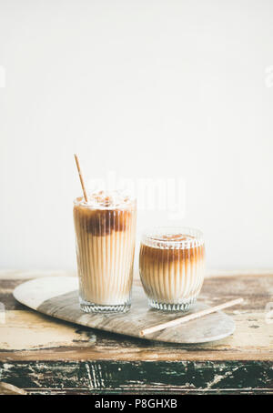Eiskaffee in hohe Gläser mit Milch und Strohhalme an Bord über Holztisch, weiße Wand im Hintergrund, kopieren. Sommer erfrischende Getränke Eis coff Stockfoto