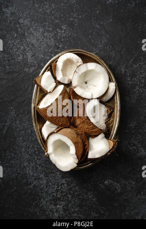Risse Kokosnüsse in metallischen Fach auf dunkel strukturierten Hintergrund angeordnet. Stockfoto