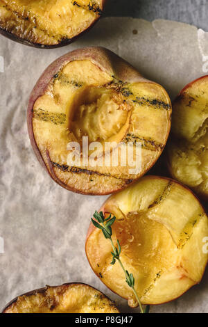 Nahaufnahme von gegrillte Pfirsiche und Nektarinen auf Backpapier Blatt mit Thymian halbiert Stockfoto