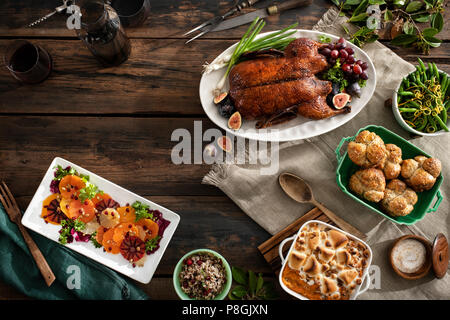 Eine Ansicht eines Urlaubs zum Abendessen mit gebratener Ente, Zitrus Salat, Reis, Bohnen, Brötchen, süsse Kartoffel Auflauf und Wein. Warme, stimmungsvolle Töne auf Stockfoto