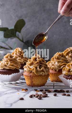 Frische hausgemachte Kuchen mit Kaffee buttercream und Gießen vom Löffel caramel stehend auf Kühlung Rack mit Eukalyptus Zweig und Kaffeebohnen Stockfoto