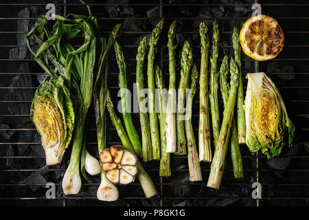 Gegrilltes Gemüse grüner Spargel, Knoblauch, Zitrone, Frühlingszwiebeln, Salat auf BBQ Grill Rack über Kohle. Ansicht von oben, Platz. Stockfoto
