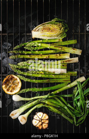 Gegrilltes Gemüse grüner Spargel, Knoblauch, Zitrone, Frühlingszwiebeln, Salat auf BBQ Grill Rack über Kohle. Ansicht von oben, Platz. Stockfoto