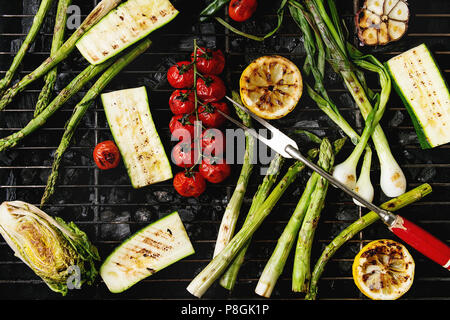 Gegrilltes Gemüse grüner Spargel, Knoblauch, Zitrone, Frühlingszwiebeln, Zucchini, Tomaten, Salat auf BBQ Grill Rack über Kohle. Ansicht von oben. Grill Stockfoto