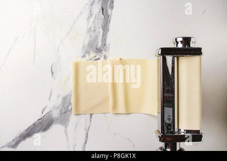 Gerollte Teig für hausgemachten italienischen Teigwaren Lasagne von Pasta Maschine Teekocher mit Grieß Mehl über weißem Marmor Textur Hintergrund. Flach, Stockfoto