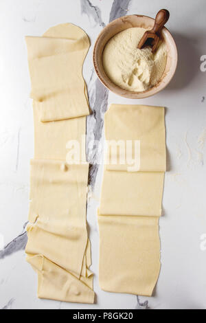 Gerollte Teig für hausgemachten italienischen Teigwaren Lasagne von Pasta Maschine Teekocher mit Grieß Mehl über weißem Marmor Textur Hintergrund. Flach, Stockfoto