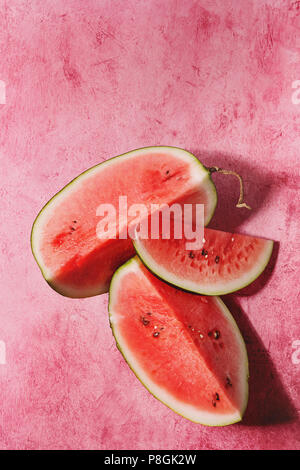 Reif in Scheiben geschnittenen Wassermelone über rosa Textur Hintergrund. Flach, Platz. Stockfoto