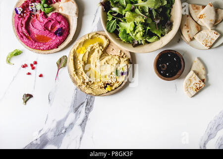 Auswahl an hausgemachten traditionellen und Rote Beete verteilt Hummus mit Pinienkernen, Olivenöl, Granatapfel auf keramischen Platten mit Fladenbrot und Grün s serviert. Stockfoto