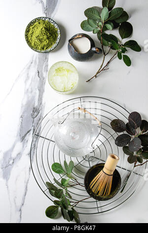 Zutaten für die Herstellung von Matcha Eis trinken. Grüner Tee matcha Pulver in Keramik Schüssel, traditionelle Bambus Löffel, Schneebesen auf Kühlung Rack, Teekanne aus Glas, Eis c Stockfoto