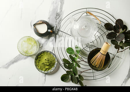 Zutaten für die Herstellung von Matcha Eis trinken. Grüner Tee matcha Pulver in Keramik Schüssel, traditionelle Bambus Löffel, Schneebesen auf Kühlung Rack, Teekanne aus Glas, Eis c Stockfoto