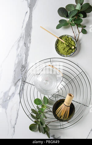 Zutaten für die Herstellung von Matcha Tee trinken. Grüner Tee matcha Pulver in Keramik Schüssel, traditionelle Bambus Löffel, Schneebesen auf Kühlung Rack, Teekanne aus Glas, grün Bh Stockfoto