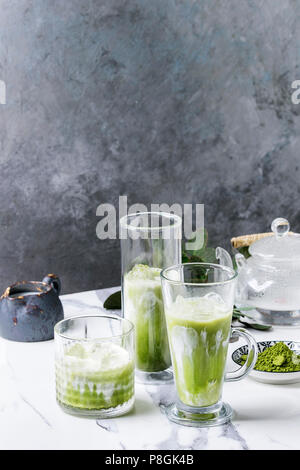 Matcha Grüntee Iced Latte oder Cocktail in drei verschiedene Gläser mit Eiswürfeln, Matcha Pulver und kanne Milch auf weißem Marmortisch, durch g eingerichtet Stockfoto