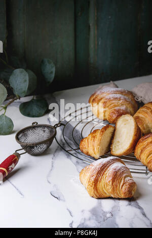 Hausgemachte Croissants und mit Zucker Puder auf Kühlung Rack geschnitten. Durch eukalyptus Zweig über weißem Marmor tisch eingerichtet. Stockfoto