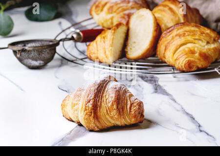 Hausgemachte Croissants und mit Zucker Puder auf Kühlung Rack geschnitten. Durch eukalyptus Zweig über weißem Marmor tisch eingerichtet. Stockfoto