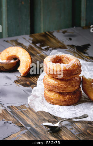 Hausgemachte Blätterteig frittierte Krapfen oder cronuts in mit Zucker auf zerknittertes Papier über dunklen Holz- beton Tisch stapeln. Stockfoto
