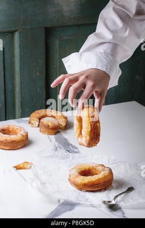 Boy's Hand halten hausgemachte Blätterteig frittierte Krapfen oder cronuts mit Zucker auf zerknittertes Papier über weißem Marmor Küchentisch. Stockfoto