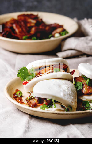 Asiatische sandwich gedämpft Gua bao Brötchen mit Schweinebauch, grünen und Gemüse in Keramik Teller am Tisch serviert mit Bettwäsche Tischdecke. Im asiatischen Stil schnell fo Stockfoto