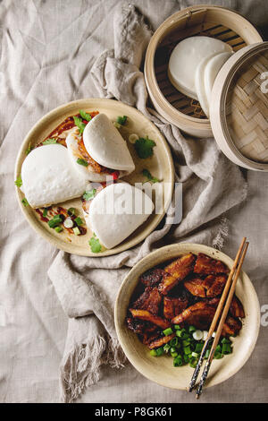 Asiatische sandwich gedämpft Gua bao Brötchen mit Schweinebauch, grünen und Gemüse in Keramik Teller über Bettwäsche Tischdecke. Im asiatischen Stil fast food Dinner Stockfoto