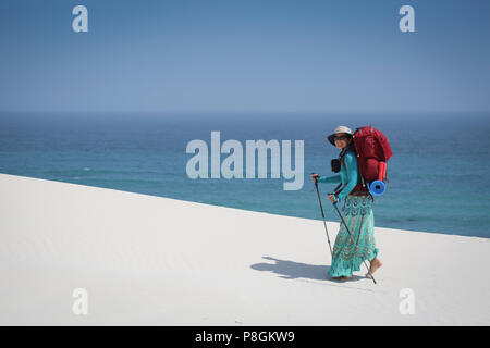 Weibliche Wanderer tragen Kleid zu Fuß auf einem weißen Düne direkt am Meer an einem sonnigen Tag. Stockfoto