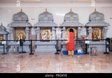 Eine Frau betend und meditierend vor Statuen der Götter und Göttinnen im hinduistischen Tempel Gesellschaft in Flushing, Queens, New York City. Stockfoto