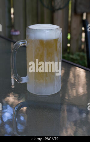 Eine frostige Becher Bier auf einem Glastisch Stockfoto